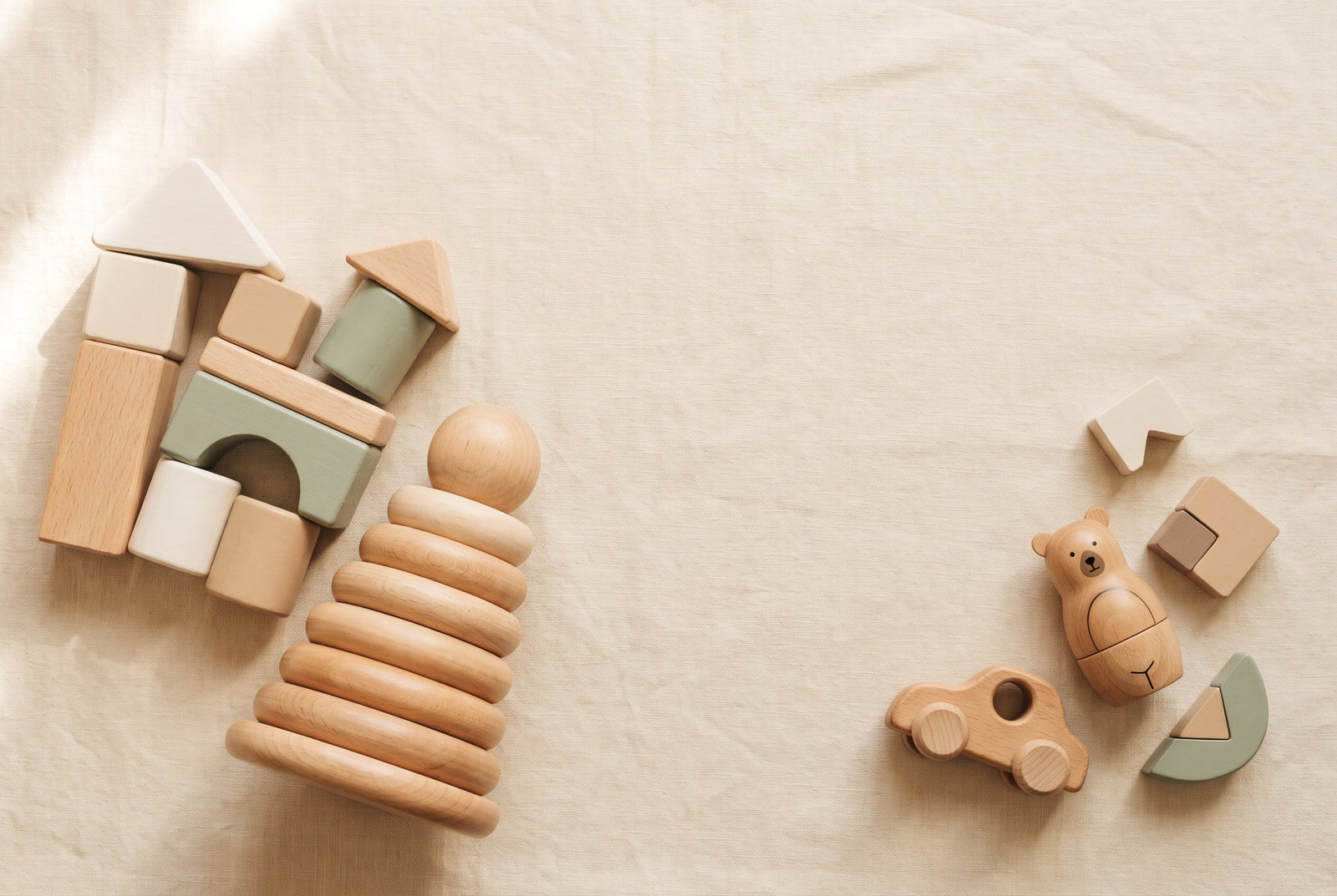 Natural wooden toddler toys grouped by size, chunky large pieces beside a few smaller pieces on cream linen