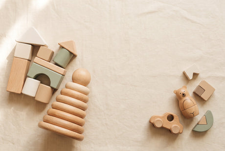 Natural wooden toddler toys grouped by size, chunky large pieces beside a few smaller pieces on cream linen