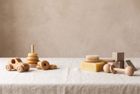 Natural wooden toys beside a block of beeswax and a small dish of oil on cream linen, illustrating natural wooden toy finishes