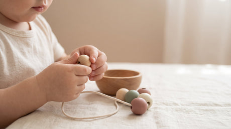 Toddler's hands threading a natural wooden lacing bead onto a cord in Montessori fine motor play