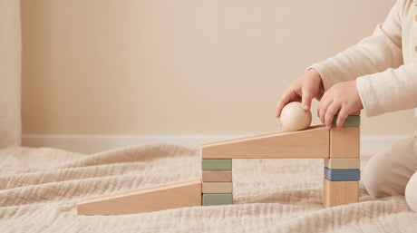 Toddler's hands rolling a wooden ball down a block ramp in early STEM cause-and-effect play