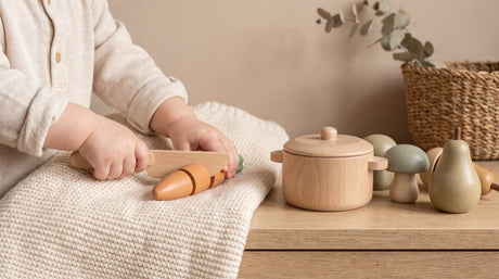Toddler's hands pretend cooking with wooden play food in imaginative Montessori play