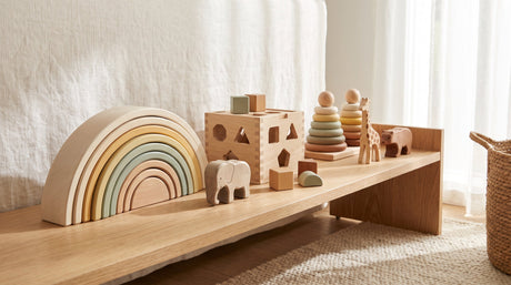 Curated collection of natural wooden Montessori toys styled on a light oak playroom shelf
