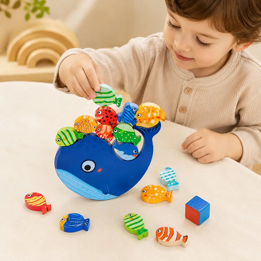 Toddler playing with the Montessori wooden whale balancing toy and patterned wooden fish