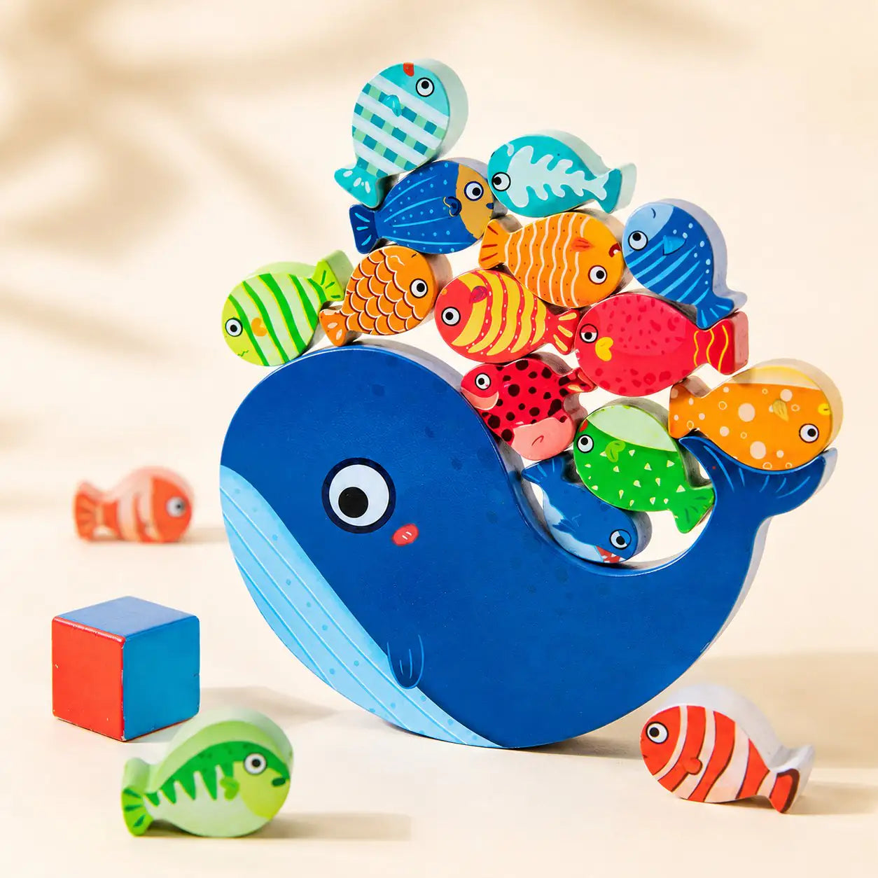 Wooden whale balancing toy with blue whale base and 14 colorful wooden fish on a cream background