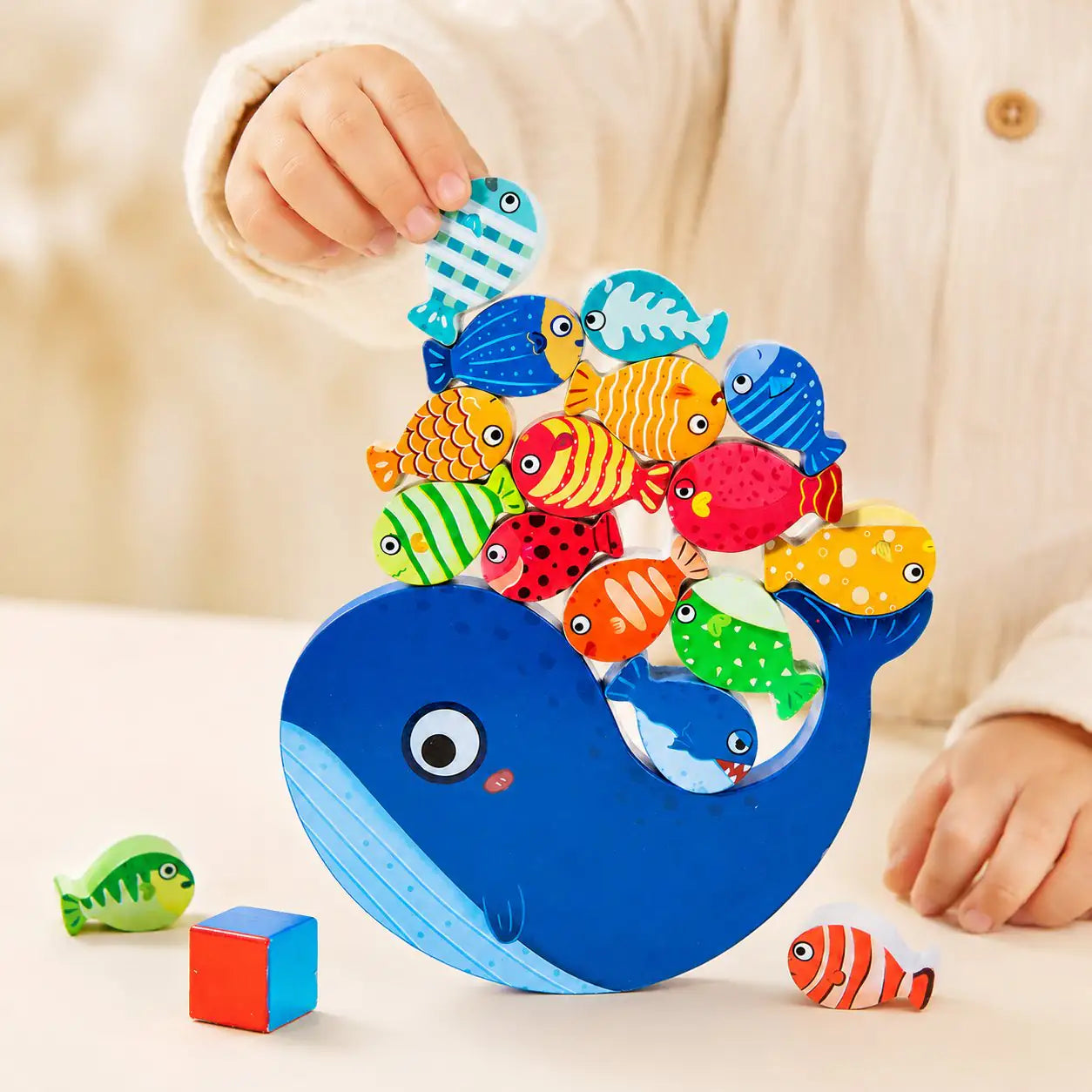 Toddler hands placing a wooden fish onto the curve of the whale balancing toy for fine motor play