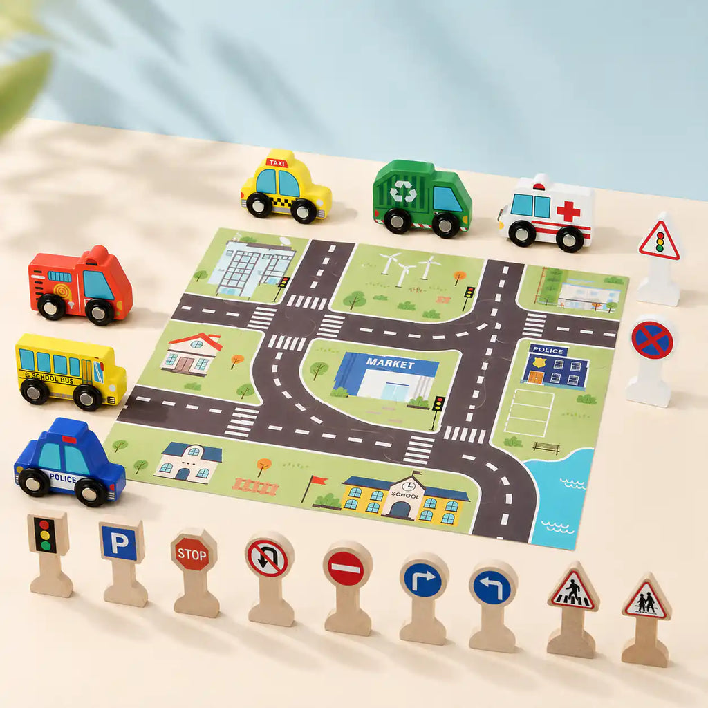Child's hand placing a wooden school bus on the printed city play mat next to ambulance, police car, and traffic signs