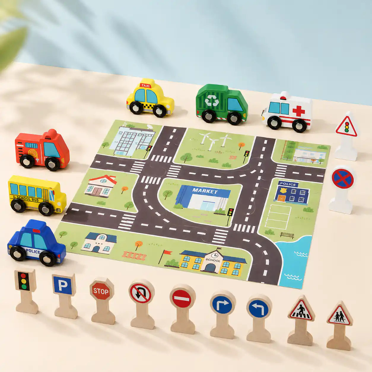Child's hand placing a wooden school bus on the printed city play mat next to ambulance, police car, and traffic signs