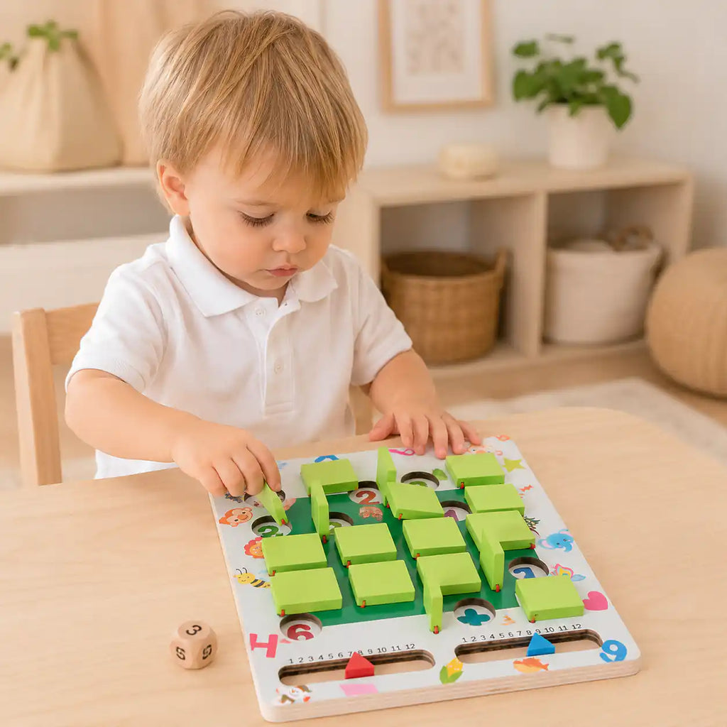 Toddler boy lifting a green sliding tile on the wooden memory game board, with a wooden number die on the table