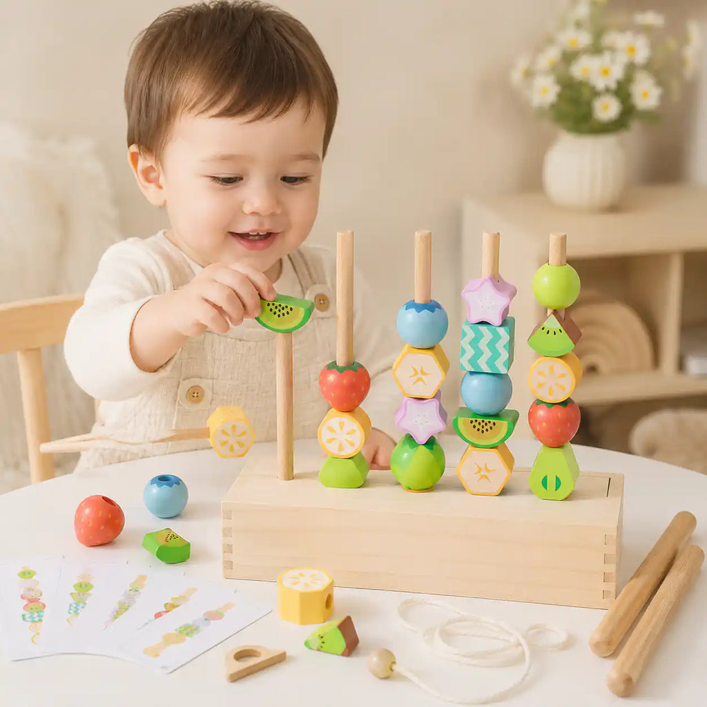 Smiling toddler placing a wooden kiwi bead onto one of four standing dowels in the wooden fruit bead stacking set