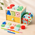 Wooden 6-in-1 Montessori activity cube with shape sorter, ABC letters, color coins, rainbow drum, and pull-through sticks on a wooden table