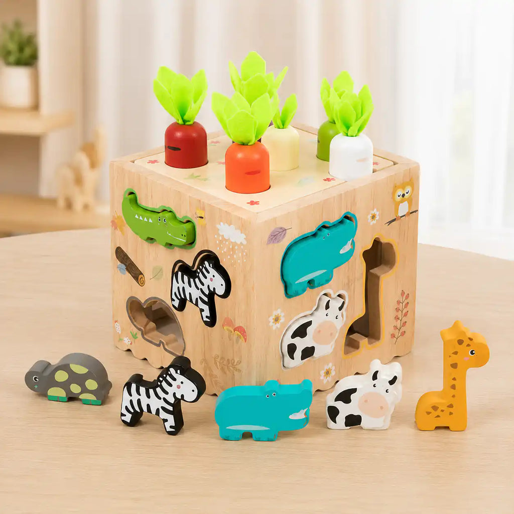 Wooden Montessori activity cube with carrot top in place and six chunky wooden animal shape-sorter pieces including turtle, zebra, hippo, cow, and giraffe lined up beside it