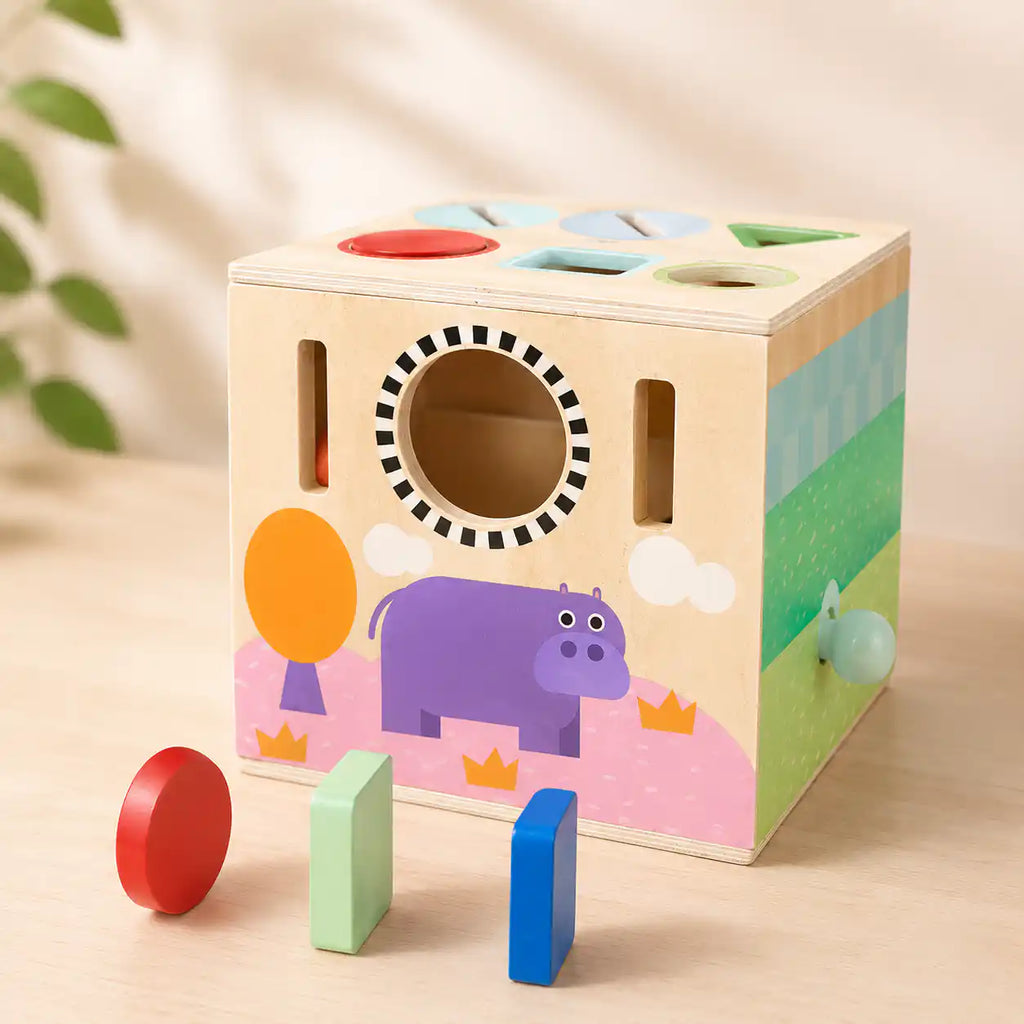 Side of wooden activity cube showing hippo illustration, peek-through hole, and shape slots for toddler play