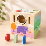 Side of wooden activity cube showing hippo illustration, peek-through hole, and shape slots for toddler play