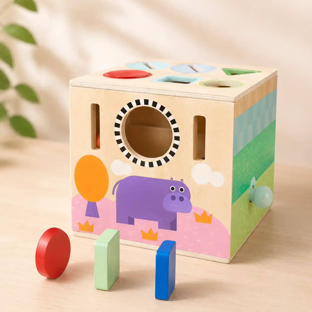 Side of wooden activity cube showing hippo illustration, peek-through hole, and shape slots for toddler play