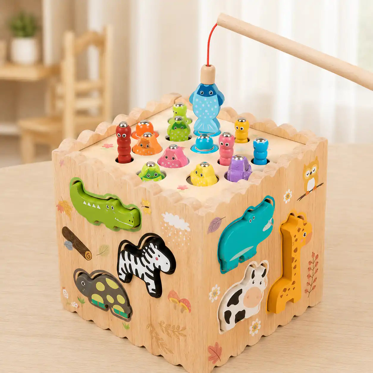 Wooden activity cube with magnetic fishing top showing colorful wooden fish and worms, with a child's hand holding the wooden fishing rod above