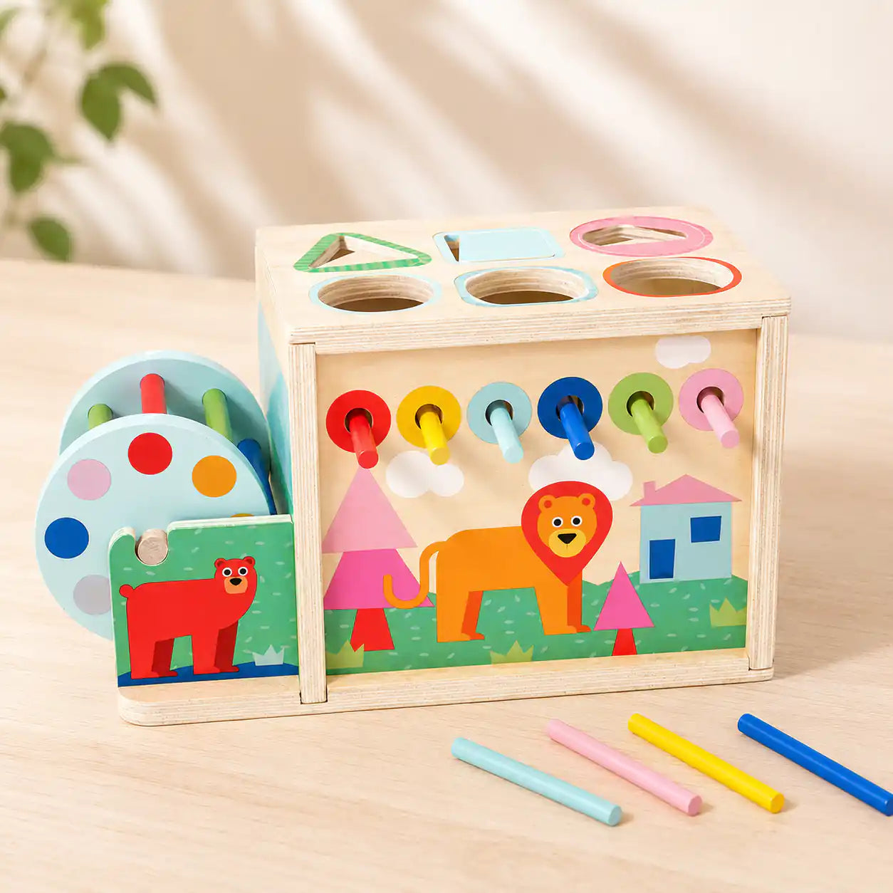 Back panel of wooden activity cube showing six rainbow pull-through sticks and a friendly lion illustration