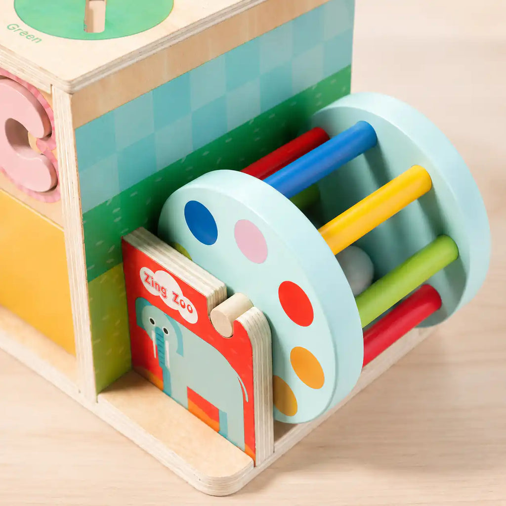 Close-up detail of wooden rainbow drum with colored sticks and Zing Zoo elephant puzzle card attached to the activity cube