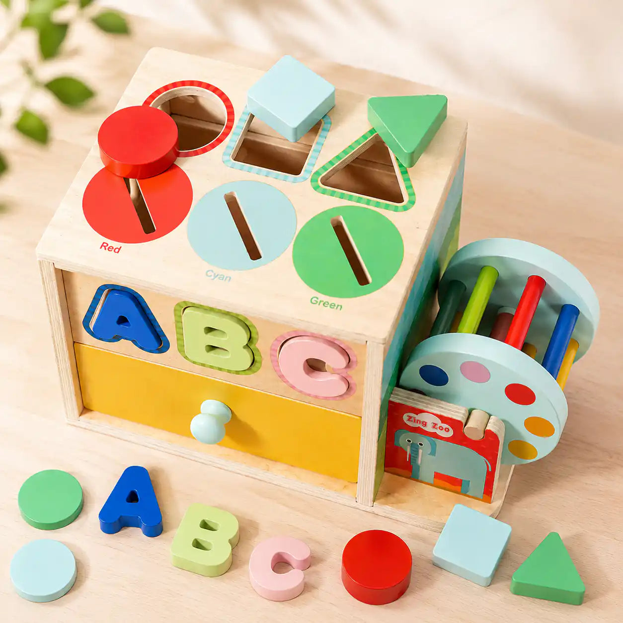 Side view of wooden 6-in-1 activity cube showing shape sorter top with Red, Cyan, Green color slots and ABC letter puzzle front