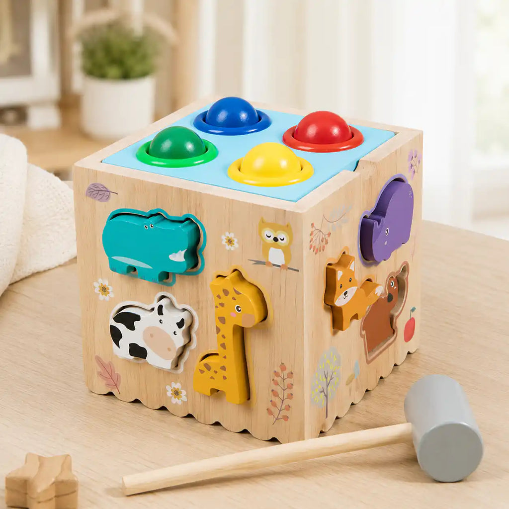 Wooden activity cube with the whack-a-mole top showing four colored half-domes, wooden mallet, and chunky animal shape-sorter pieces on the sides