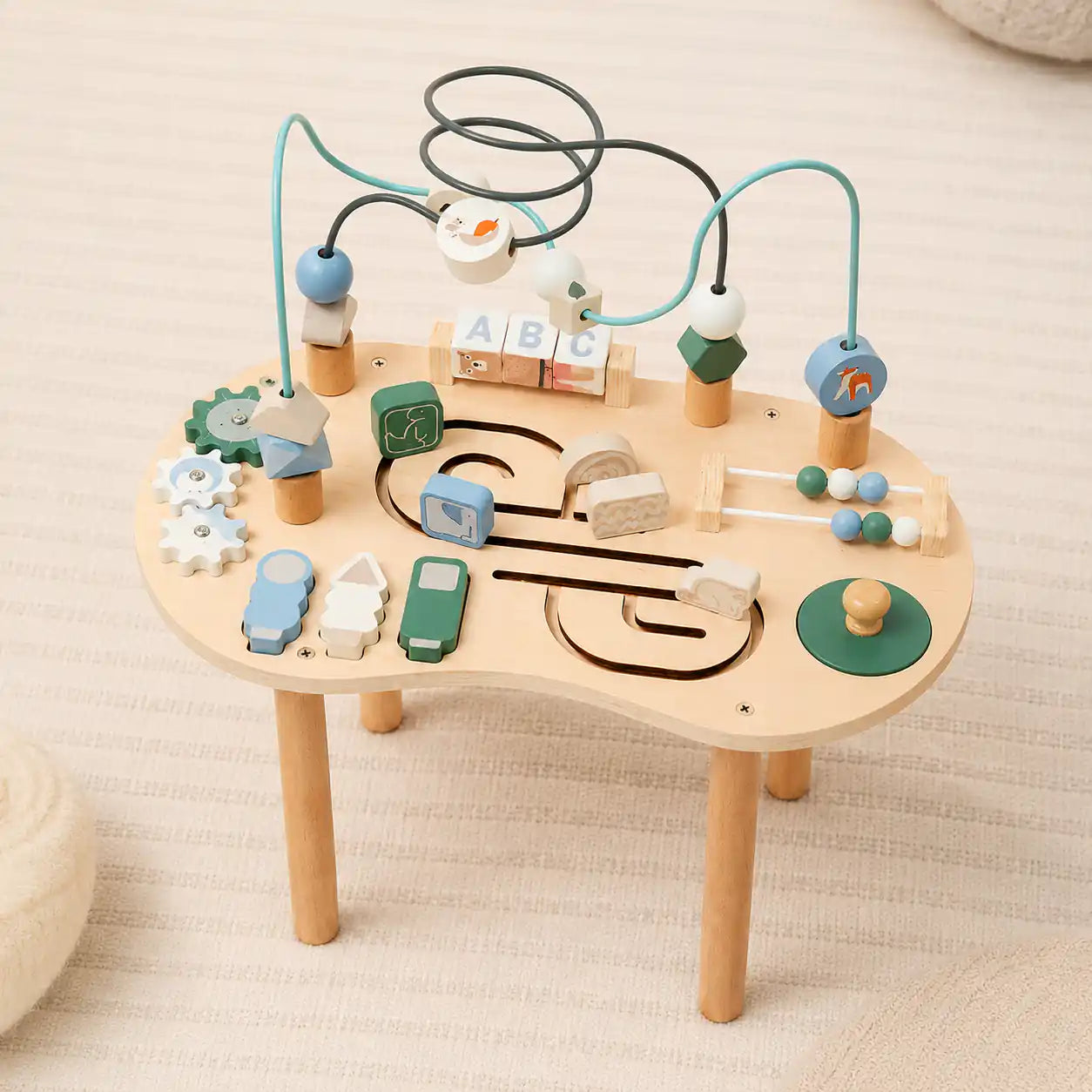 Close-up of wooden activity table top showing bead maze loops, spinning gears, and rotating alphabet blocks