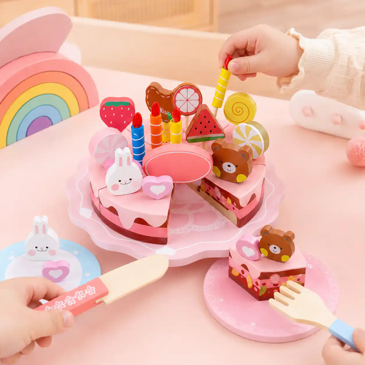 Child's hands placing colorful candles into a wooden pretend play birthday cake on a pink table