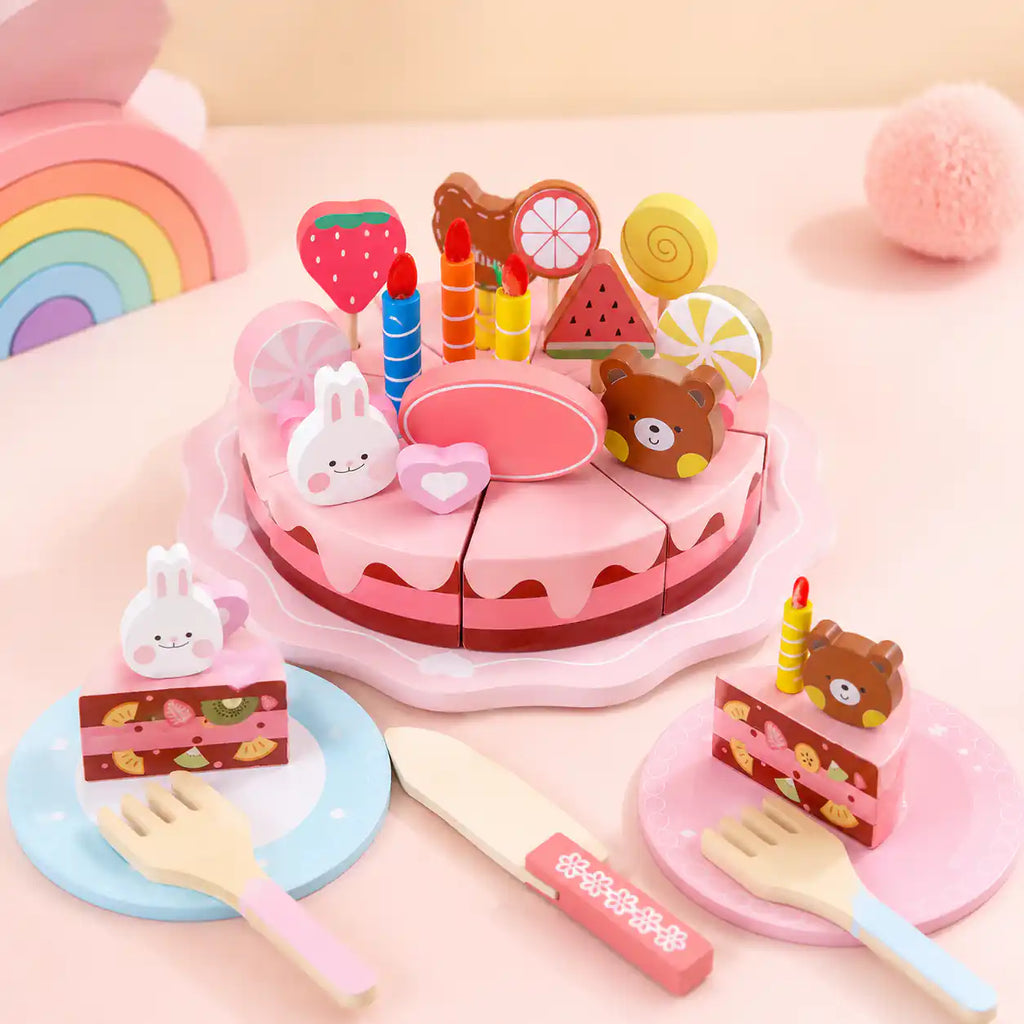 Wooden pretend play birthday cake set with two plated slices, candles, and fruit toppers on a soft pink surface