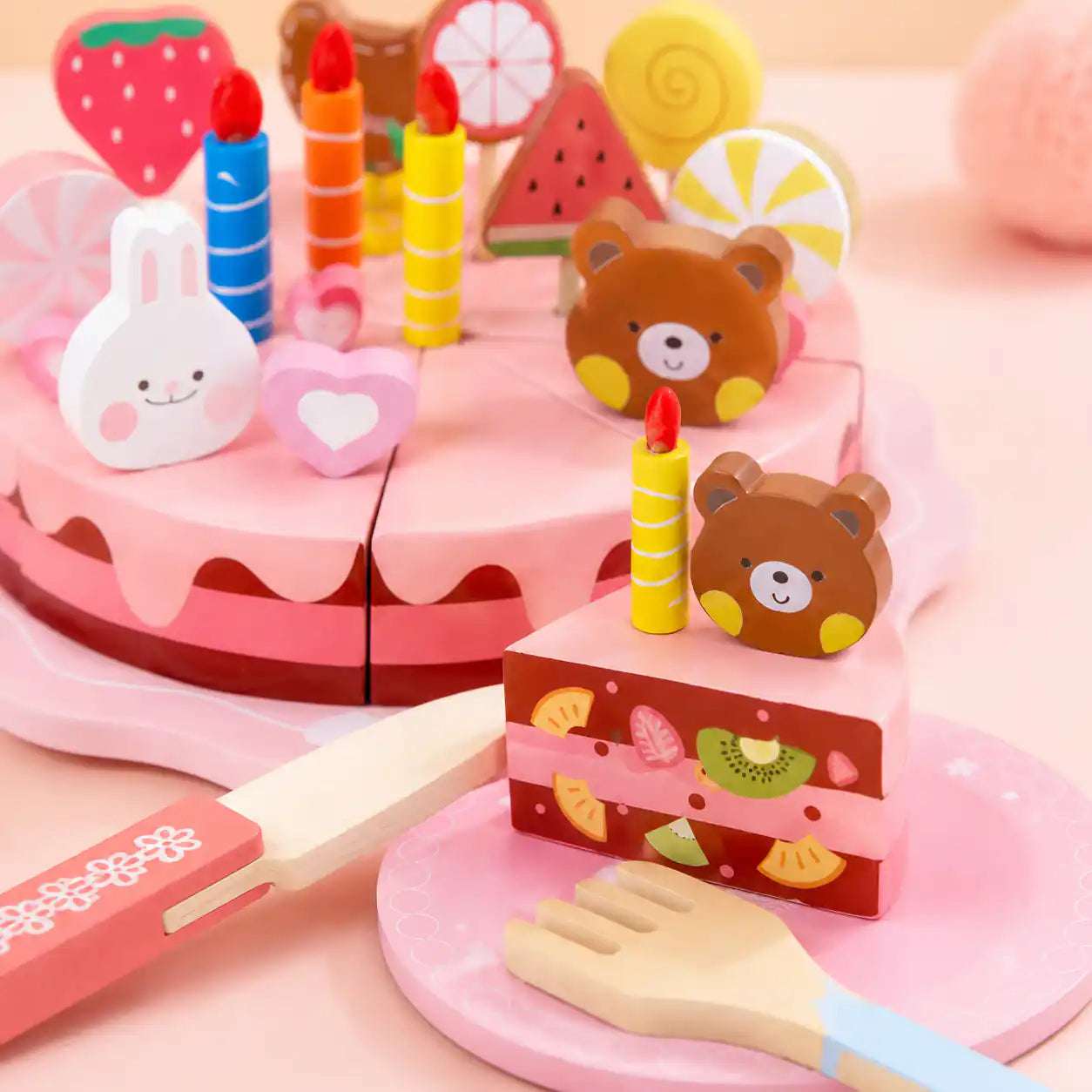 Close-up of a wooden cake slice topped with a bear and yellow candle, beside the decorated cake