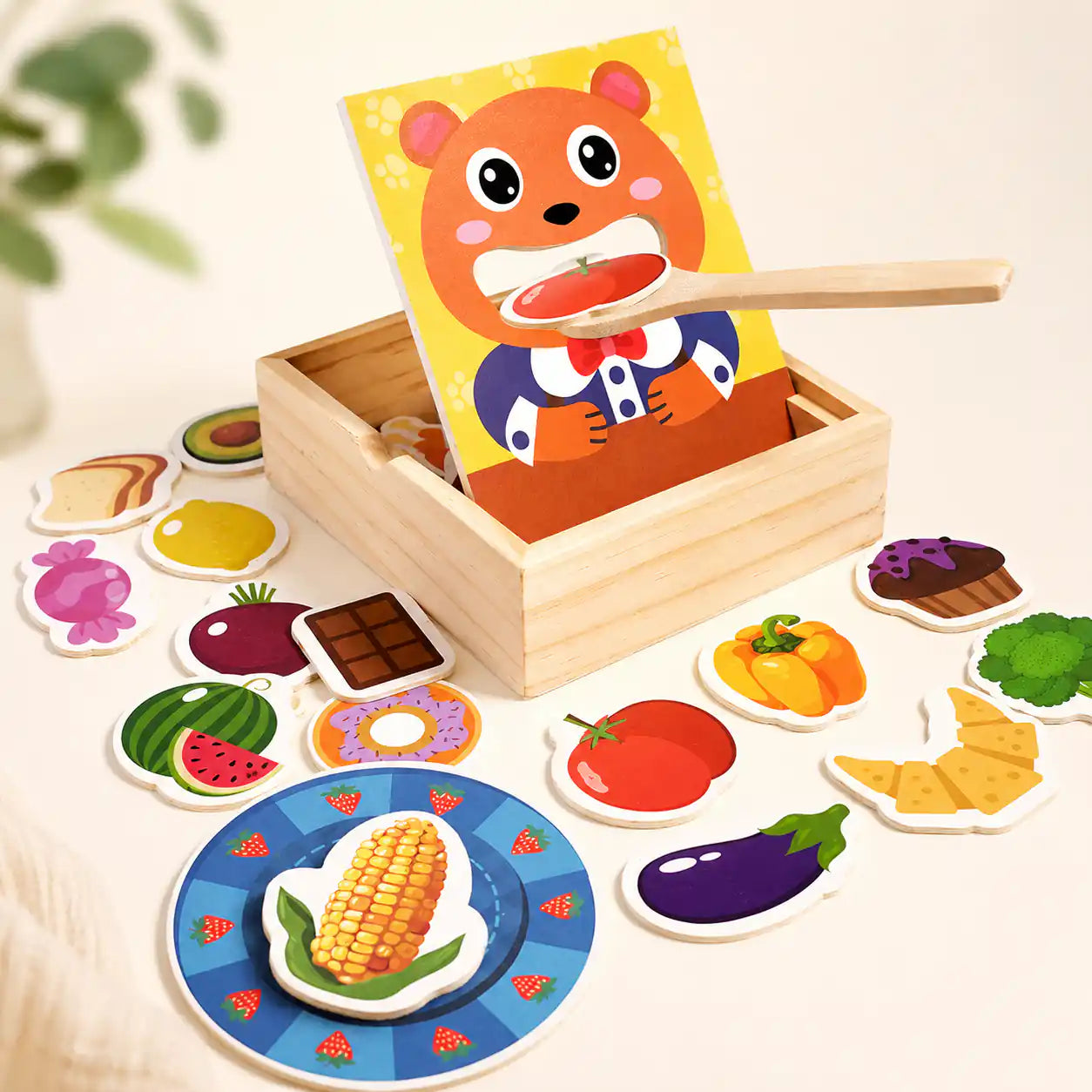 Wooden feed the bear pretend play toy with smiling bear panel, wooden spoon scooping a tomato slice, and assorted wooden food pieces on a cream background