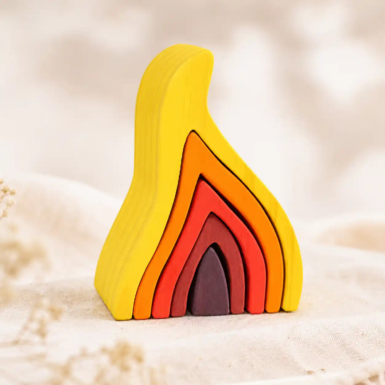 Wooden flame nesting puzzle fully assembled on a textured linen surface with soft natural light