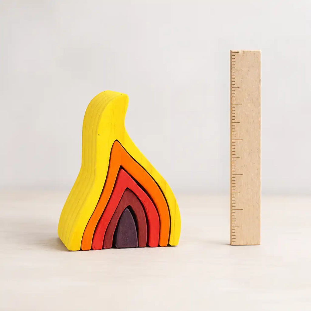 Wooden flame stacking puzzle shown next to a wooden ruler for size reference, approximately 16 to 17 centimeters tall
