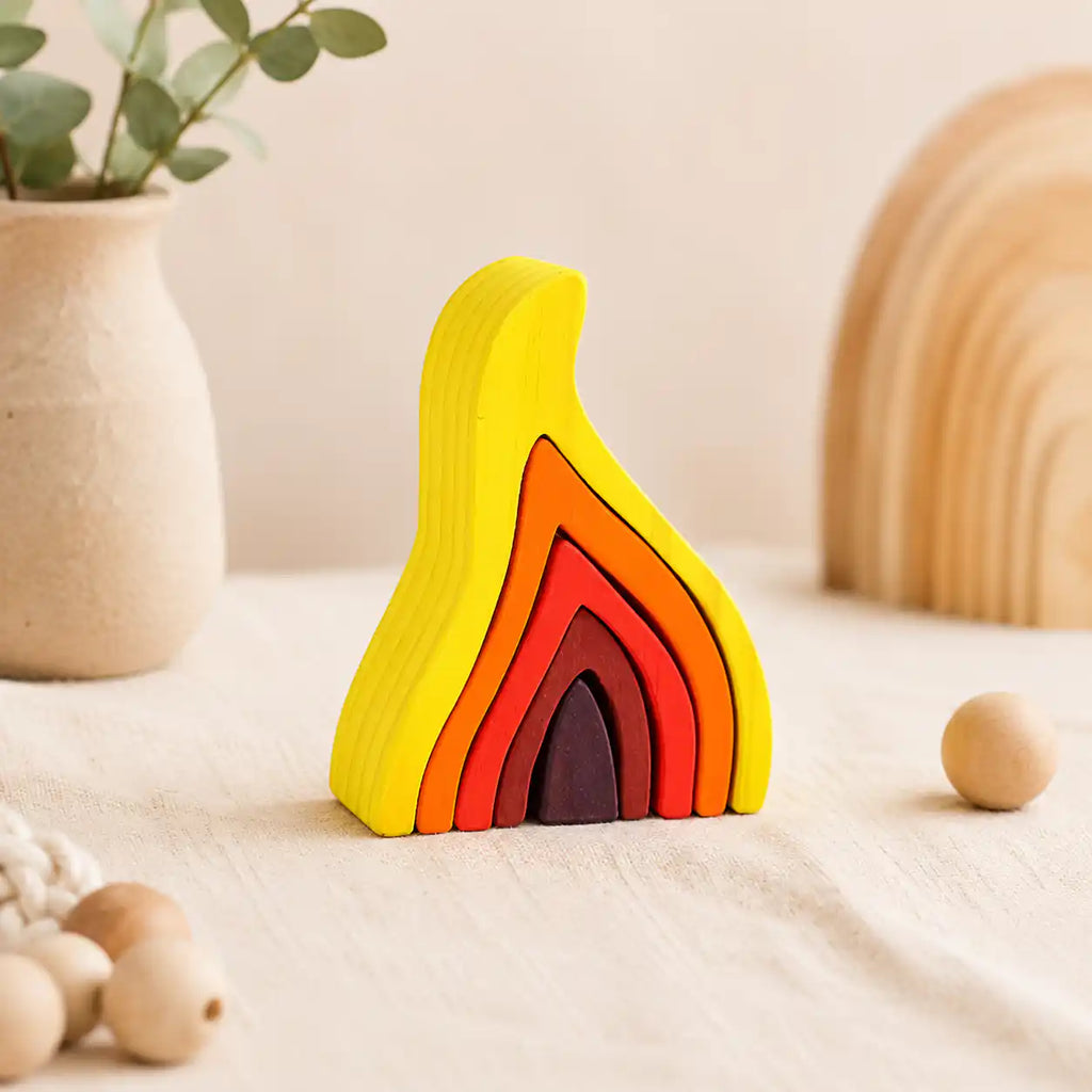 Wooden flame puzzle styled on a neutral table with a ceramic vase, wooden beads, and dried eucalyptus
