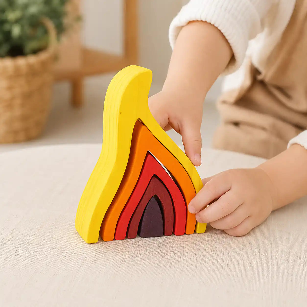 Child's hands fitting the outer yellow flame piece into the wooden Waldorf nesting puzzle on a soft surface