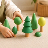Small hands placing wooden trees into a forest play scene on a warm neutral surface