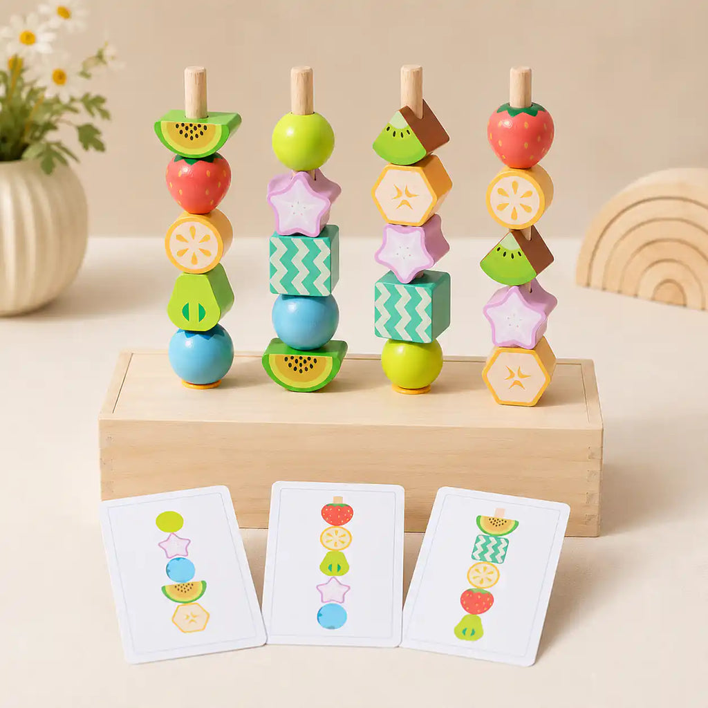 Four wooden dowels with stacked fruit beads on a wooden box base, with three pattern cards leaning in front showing bead sequences