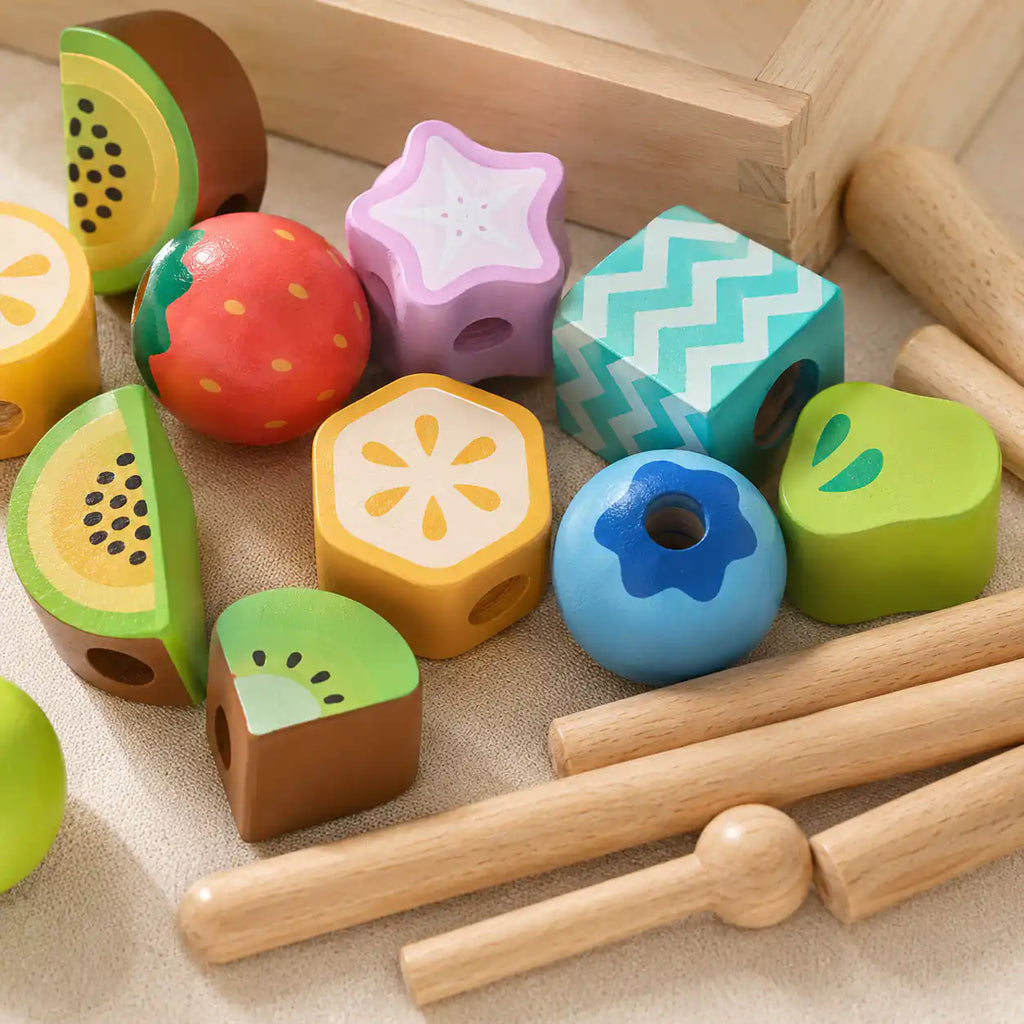 Close-up of wooden fruit beads in assorted shapes including kiwi, strawberry, star fruit, lemon hexagon, watermelon, pear, and patterned cube
