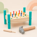 Wooden hammer and peg pounding bench with 14 colorful pegs upright, soft-headed hammer, and wooden punch tool on a cream nursery background with pastel cloud and rainbow shapes
