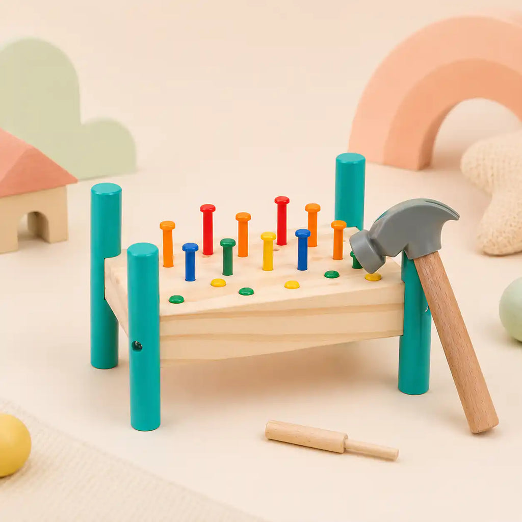 Wooden hammer and peg pounding bench styled in a Montessori-inspired playroom with pastel cloud, rainbow, and house-shaped wooden toys