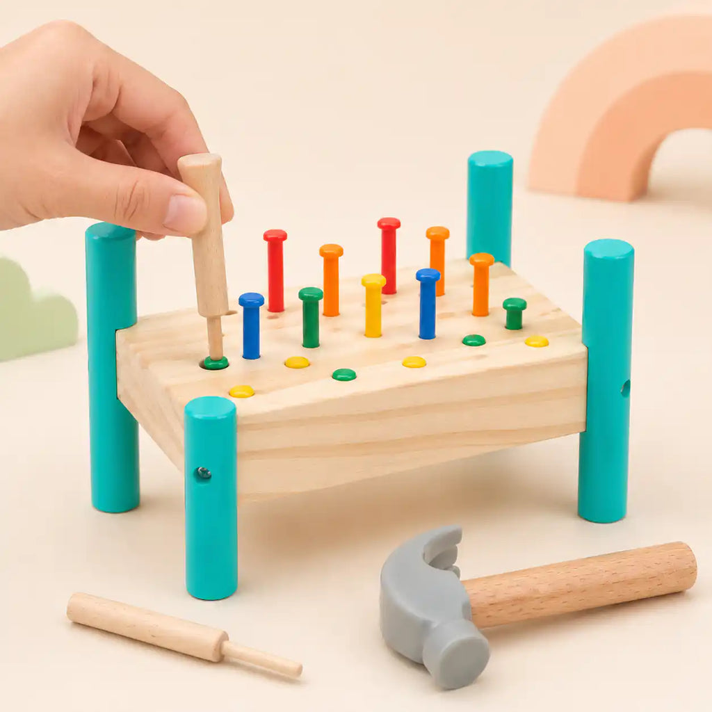 Child's hand using a wooden punch tool on a colored peg in the hammer and peg pounding bench, with a soft-headed hammer in the foreground
