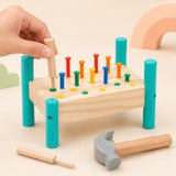 Child's hand using a wooden punch tool on a colored peg in the hammer and peg pounding bench, with a soft-headed hammer in the foreground