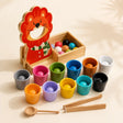 Wooden lion color sorter with 12 colored balls, cups, scoop and tongs on a cream background