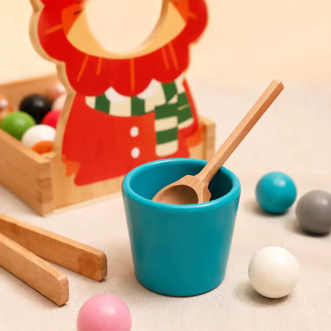 Wooden tongs pinching a colored ball into a matching cup on the lion color sorter