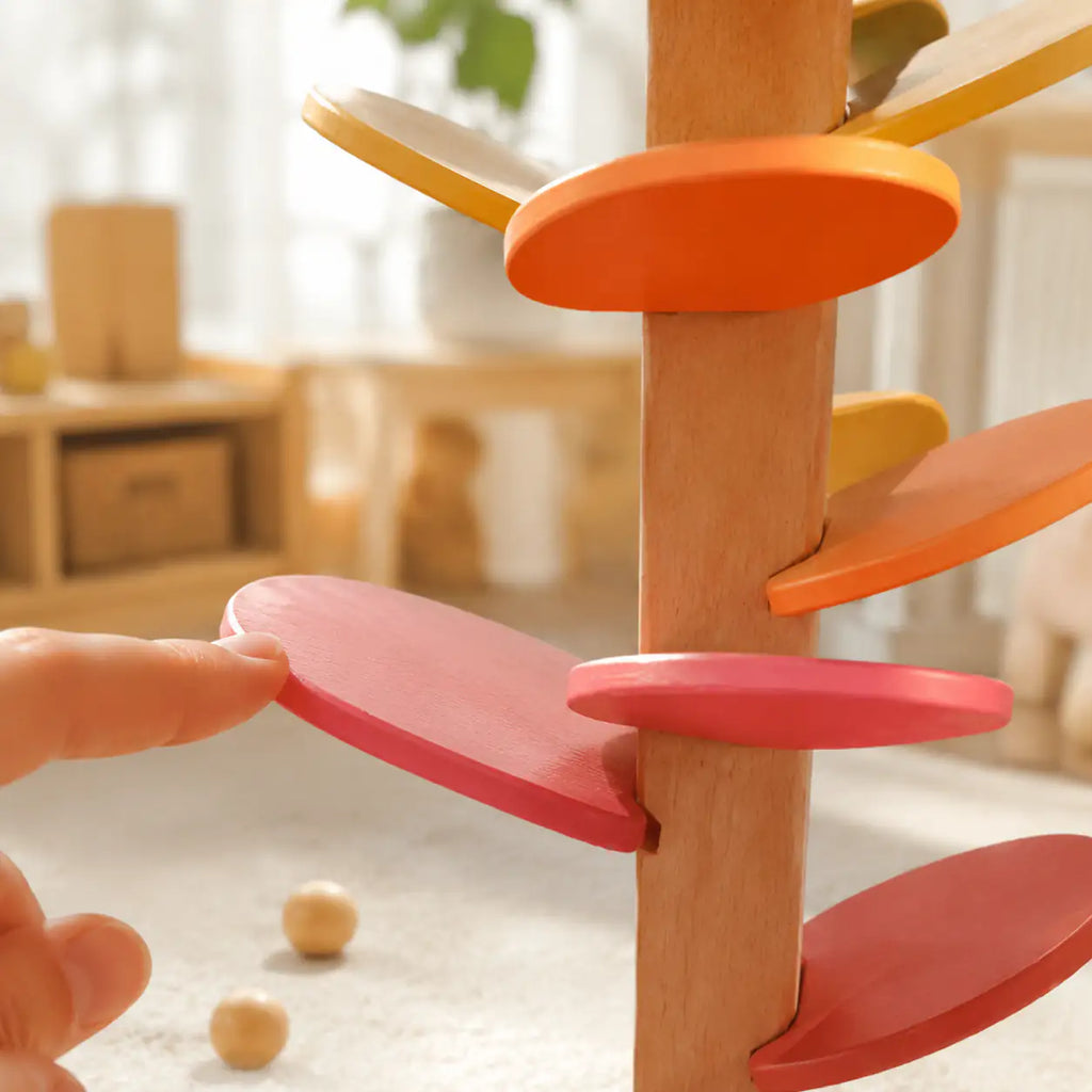 Toddler hands placing a marble at the top of the wooden marble run music tree