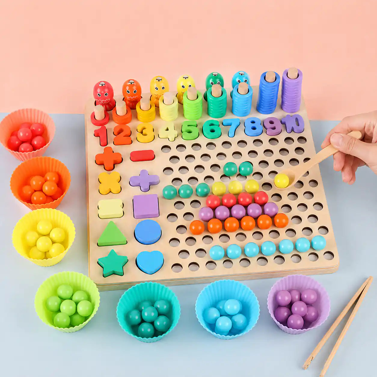 Hand using a wooden spoon to place a colored bead on the wooden Montessori 10-in-1 learning board with sorting bowls and shape pieces