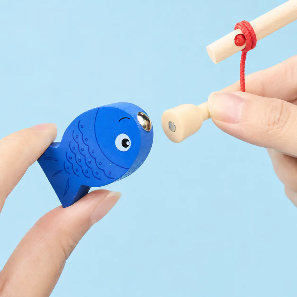 Toddler hands stacking shape pieces and casting the magnetic fishing rod on the wooden board