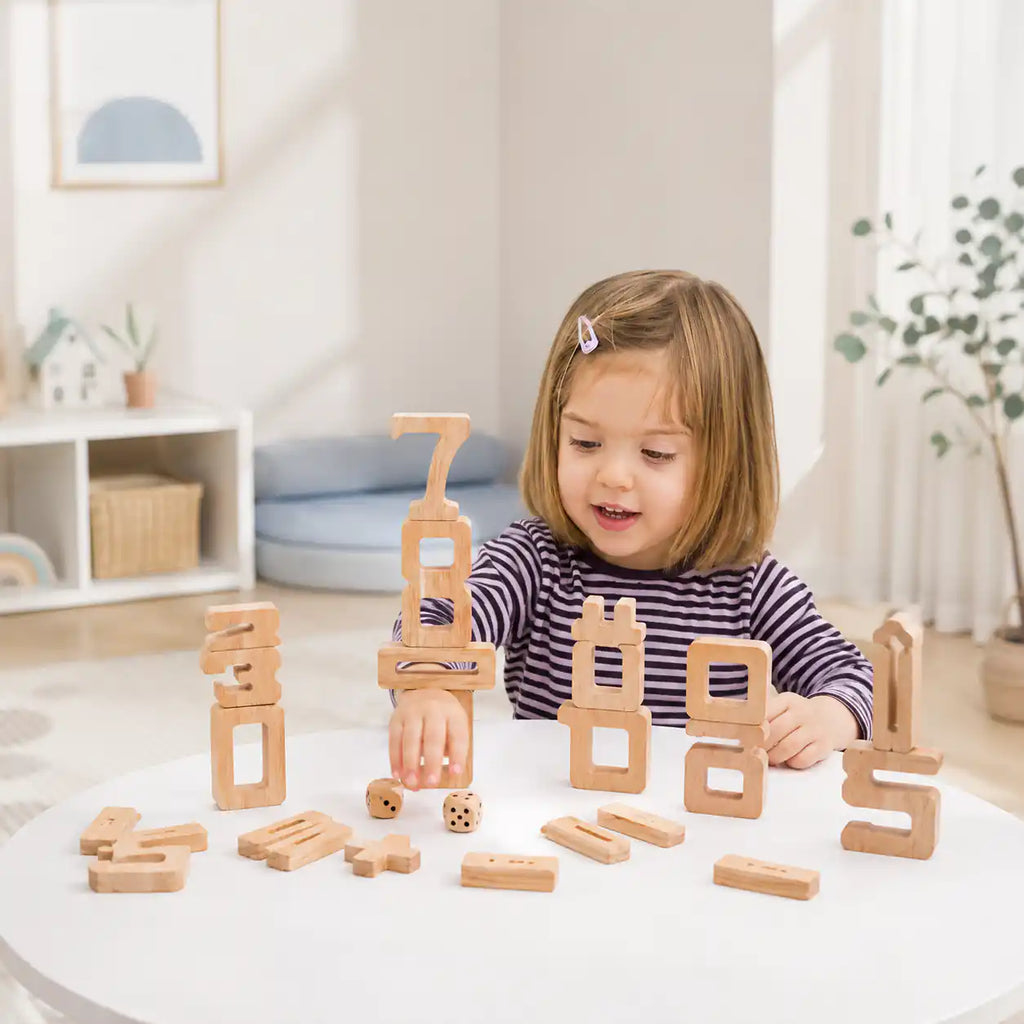 Tall sculptural tower of natural wood stacking number blocks 0 to 10 with math operator pieces and wooden dice arranged below