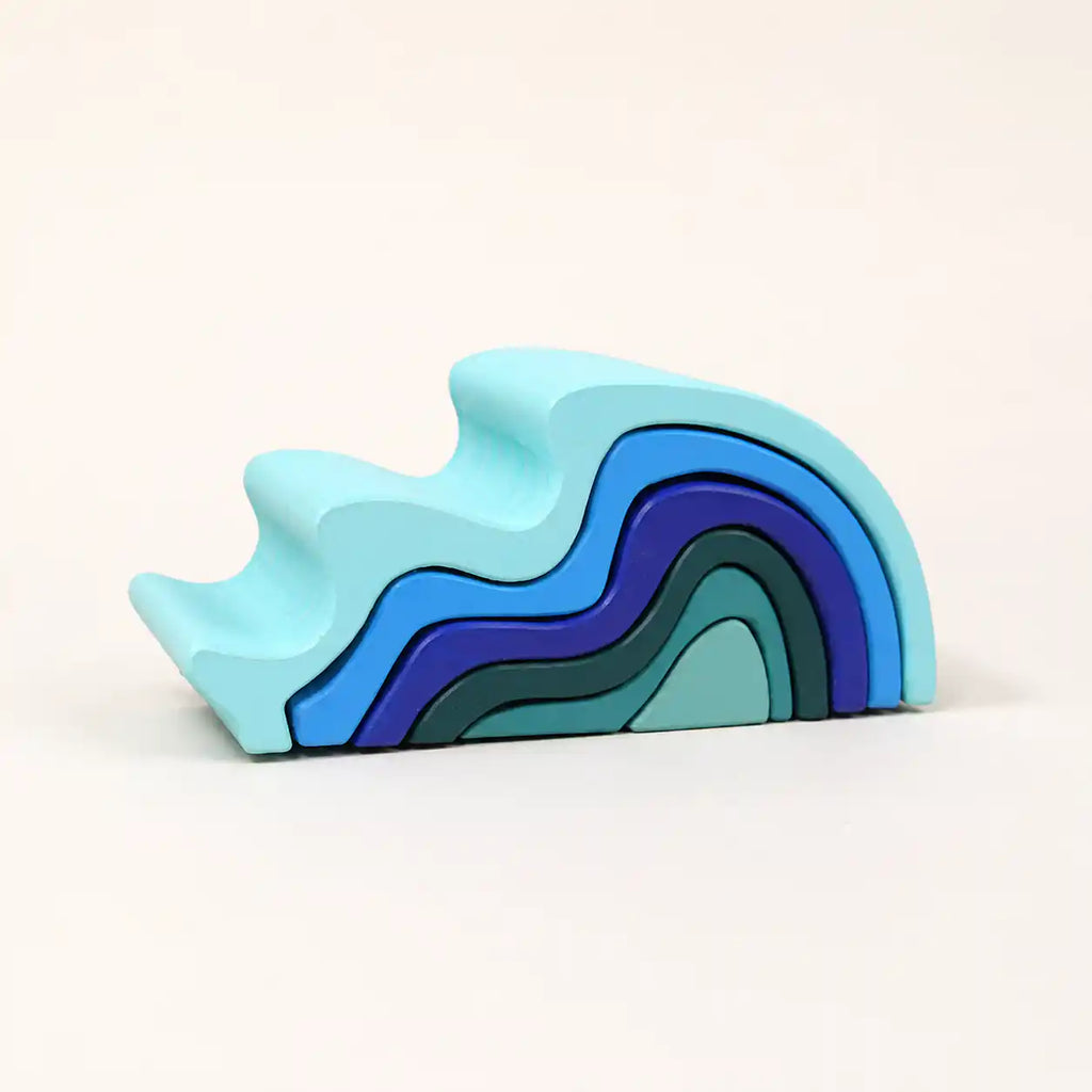 Wooden ocean wave stacker with curved wave-shaped pieces assembled on a soft cream surface, hero shot