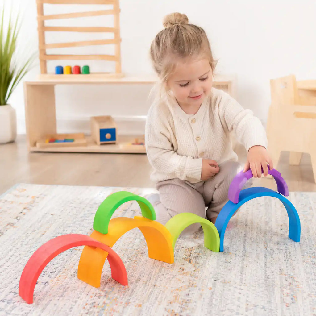 Toddler playing with large wooden rainbow arch stackers — a complementary Waldorf-inspired toy to the rainbow semicircles