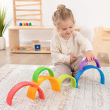 Toddler playing with large wooden rainbow arch stackers — a complementary Waldorf-inspired toy to the rainbow semicircles
