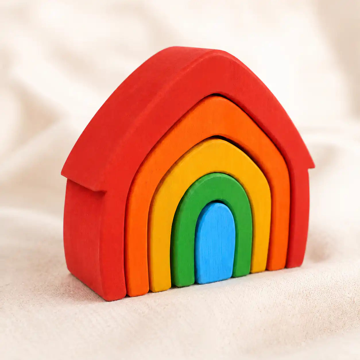 Small hands placing a wooden rainbow arch onto the stacker on a warm neutral surface